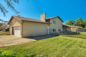 Rear view of property featuring brick siding, driveway, an attached garage, and a chimney