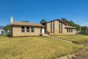 View of front of home featuring a front lawn, brick siding, a chimney, and roof with shingles
