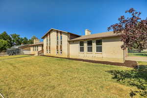 Back of house with a chimney, brick siding, and a yard
