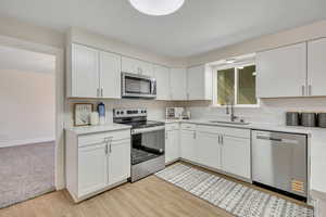 Kitchen featuring stainless steel appliances, white cabinets, light wood-type flooring, and light stone counters