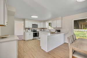 Kitchen with a peninsula, stainless steel appliances, white cabinetry, light stone countertops, and light wood-type flooring