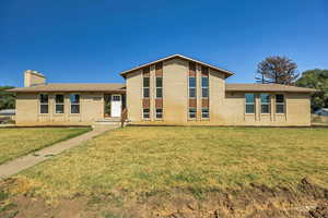 View of front of house featuring brick siding, a front lawn, a chimney, and roof with shingles