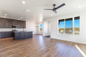 Kitchen with open floor plan, an island with sink, stainless steel appliances, dark brown cabinetry, and recessed lighting