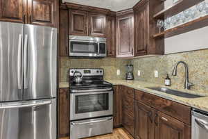 Kitchen featuring stainless steel appliances, dark brown cabinets, light stone counters, and decorative backsplash