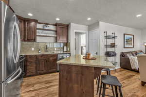 Kitchen featuring stainless steel appliances, open floor plan, dark brown cabinets, light wood finished floors, and recessed lighting