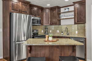 Kitchen featuring stainless steel appliances, dark brown cabinetry, open shelves, a center island, and a breakfast bar area