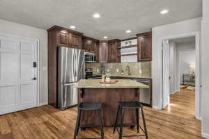 Kitchen with open shelves, appliances with stainless steel finishes, dark brown cabinets, light stone counters, and a kitchen island