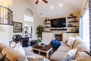 Carpeted living room featuring high vaulted ceiling, french doors, a stone fireplace, and ceiling fan