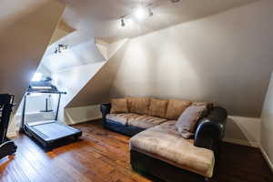 Living area with rail lighting, lofted ceiling, and hardwood / wood-style floors