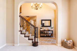 Entryway with arched walkways, light carpet, a chandelier, and lofted ceiling