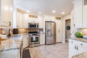 Kitchen with tasteful backsplash, stainless steel appliances, light stone countertops, white cabinetry, and recessed lighting