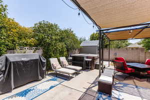 Fenced backyard featuring a patio area, a grill, a storage unit, and a hot tub