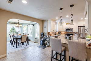 Kitchen featuring light stone counters, hanging light fixtures, arched walkways, a kitchen breakfast bar, and appliances with stainless steel finishes