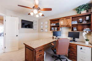 Office with a wainscoted wall, built in desk, a ceiling fan, and light carpet