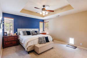 Carpeted bedroom with a raised ceiling and ceiling fan