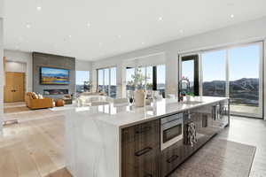 Kitchen with a large fireplace, light wood finished floors, a spacious island, light stone countertops, and recessed lighting