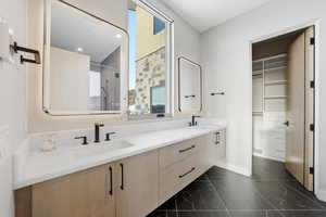 Bathroom featuring double vanity, a stall shower, dark marble finish flooring, and a walk in closet