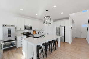 Kitchen featuring appliances with stainless steel finishes, a kitchen bar, light wood finished floors, white cabinets, and recessed lighting
