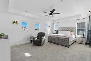 Bedroom with a raised ceiling, light carpet, and ceiling fan