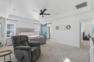 Bedroom featuring a tray ceiling, a barn door, light carpet, and multiple windows