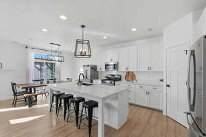 Kitchen with a center island with sink, stainless steel appliances, a kitchen breakfast bar, recessed lighting, and decorative light fixtures