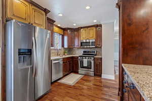 Kitchen featuring stainless steel appliances, dark wood finished floors, light stone counters, tasteful backsplash, and recessed lighting