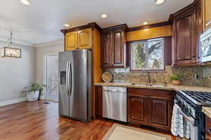 Kitchen featuring appliances with stainless steel finishes, light stone counters, ornamental molding, pendant lighting, and light wood-style floors