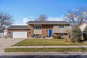 Raised ranch with a front lawn, driveway, an attached garage, and brick siding