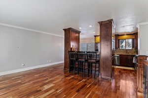 Bar area with crown molding, dark wood-style flooring, dark brown cabinetry, decorative backsplash, and recessed lighting