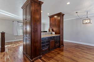 Kitchen with dark wood-type flooring, dark brown cabinetry, ornamental molding, light stone countertops, and hanging light fixtures