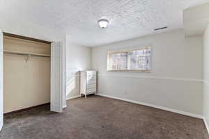 Unfurnished bedroom featuring a textured ceiling, dark colored carpet, and a closet
