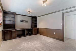 Unfurnished living room featuring wainscoting, a textured ceiling, carpet flooring, ornamental molding, and wooden walls