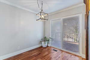 Unfurnished dining area featuring wood finished floors, ornamental molding, and a chandelier