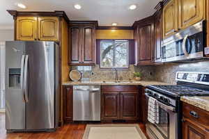 Kitchen featuring stainless steel appliances, dark wood finished floors, dark brown cabinetry, crown molding, and decorative backsplash