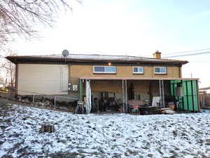 Snow covered property featuring a patio, a chimney, and brick siding