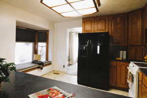 Kitchen with dark countertops, black refrigerator with ice dispenser, white electric stove, and brown cabinets