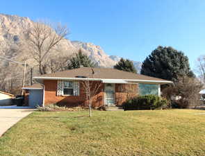 Ranch-style home featuring a front lawn, brick siding, concrete driveway, and a mountain view