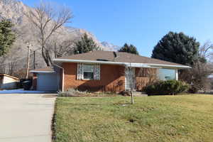 Single story home with brick siding, a front yard, a mountain view, a driveway, and a 1-car garage