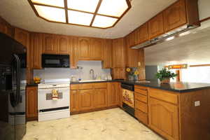 Kitchen with light flooring, brown cabinets, black appliances, a textured ceiling