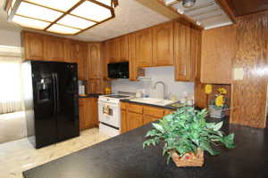 Kitchen featuring brown cabinetry, black appliances, and dark countertops