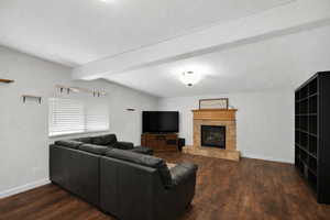 Living area with a tile fireplace, dark wood-style floors, and beam ceiling