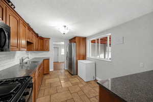Kitchen featuring dark stone countertops, black appliances, stone tile flooring, wood finish cabinetry, and a textured ceiling