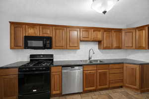 Kitchen with black appliances, wood finish cabinetry, dark stone counters, decorative backsplash, and a textured ceiling