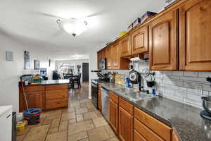 Kitchen with brown cabinets, black appliances, tasteful backsplash, and stone tile flooring