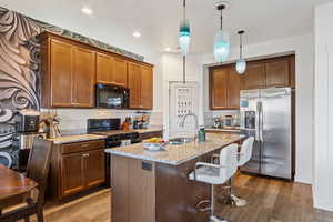 Kitchen featuring black appliances, a breakfast bar area, light stone counters, backsplash, and pendant lighting