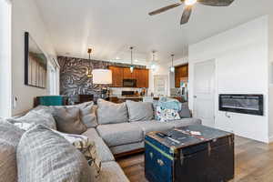 Living room featuring dark wood-type flooring, a ceiling fan, an accent wall, and recessed lighting