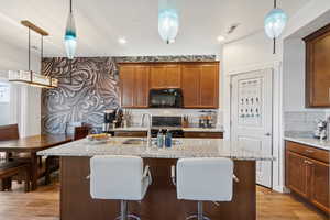Kitchen featuring hanging light fixtures, light stone counters, brown cabinetry, a kitchen breakfast bar, and recessed lighting