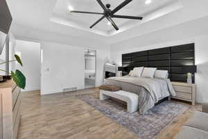 Bedroom featuring a tray ceiling, recessed lighting, ceiling fan, ensuite bath, and light wood-type flooring