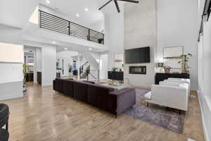 Living room featuring a tile fireplace, a towering ceiling, stairway, light wood-type flooring, and recessed lighting