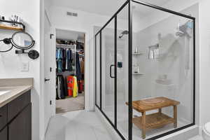 Bathroom with vanity, a walk in closet, a shower stall, and light tile patterned floors